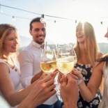 Article thumbnail: Group of friends having drinks at sunset. They are celebrating with a wine toast. They are drinking white wine. They are smiling, laughing and having fun.