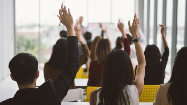 Article thumbnail: Raised up hands and arms of large group in seminar class room at Conference